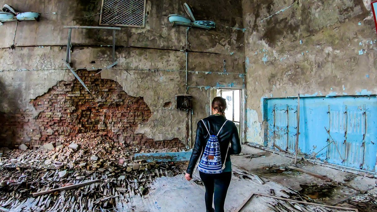 Girl in black outfit walks around the rotten floor in an abandoned sports hall in Pripyat, Ukraine