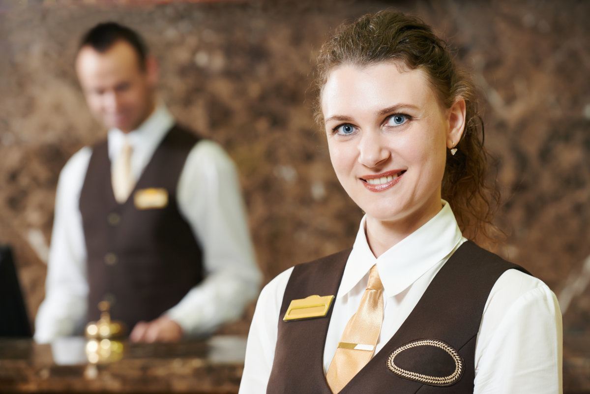 Happy Female Receptionist Worker Standing At Hotel Counter