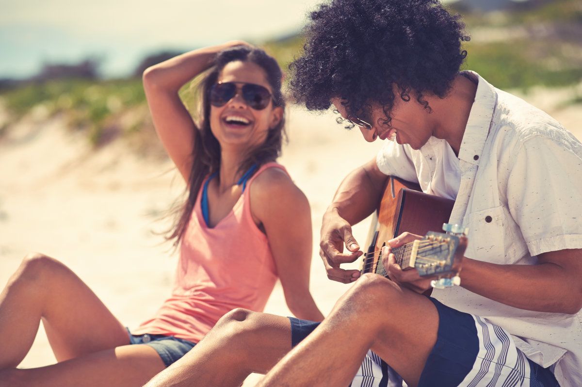 Cute Hispanic Couple Playing Guitar Serenading On Beach