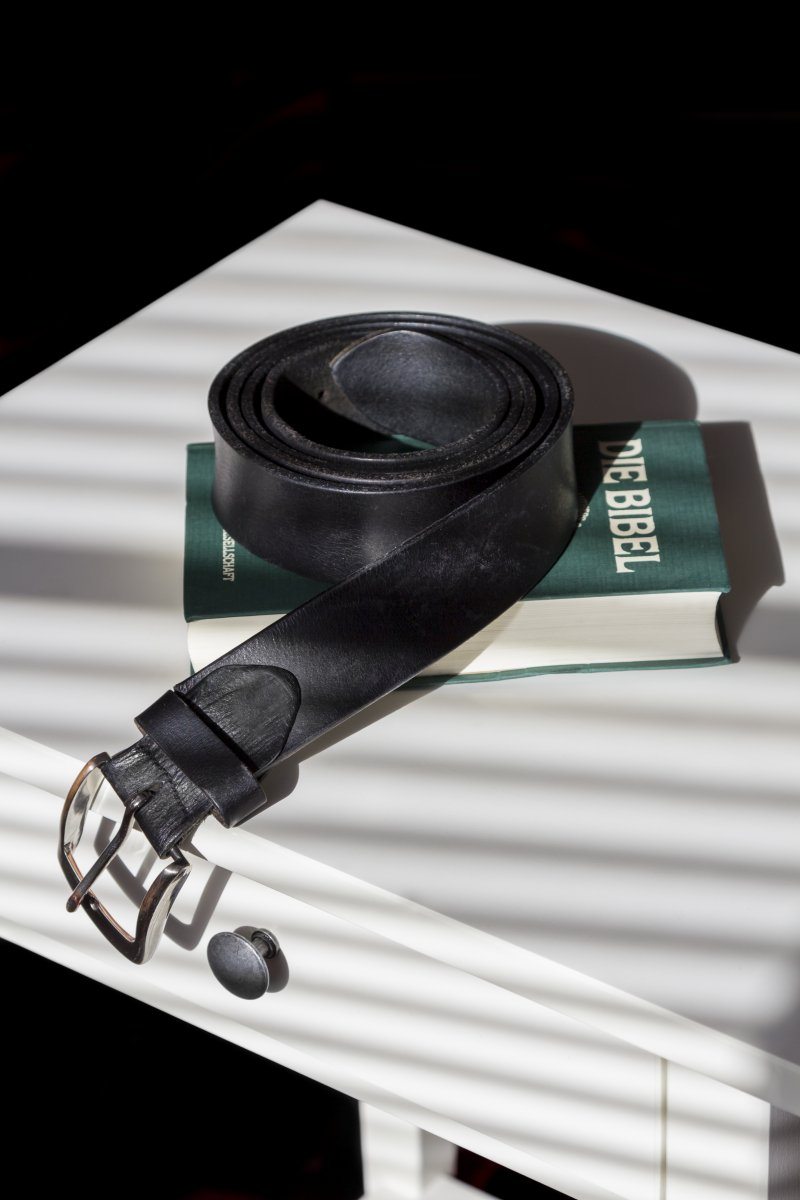 Holy Bible And A Black Leather Belt On A Night Table With Shadowing Through Jalousie