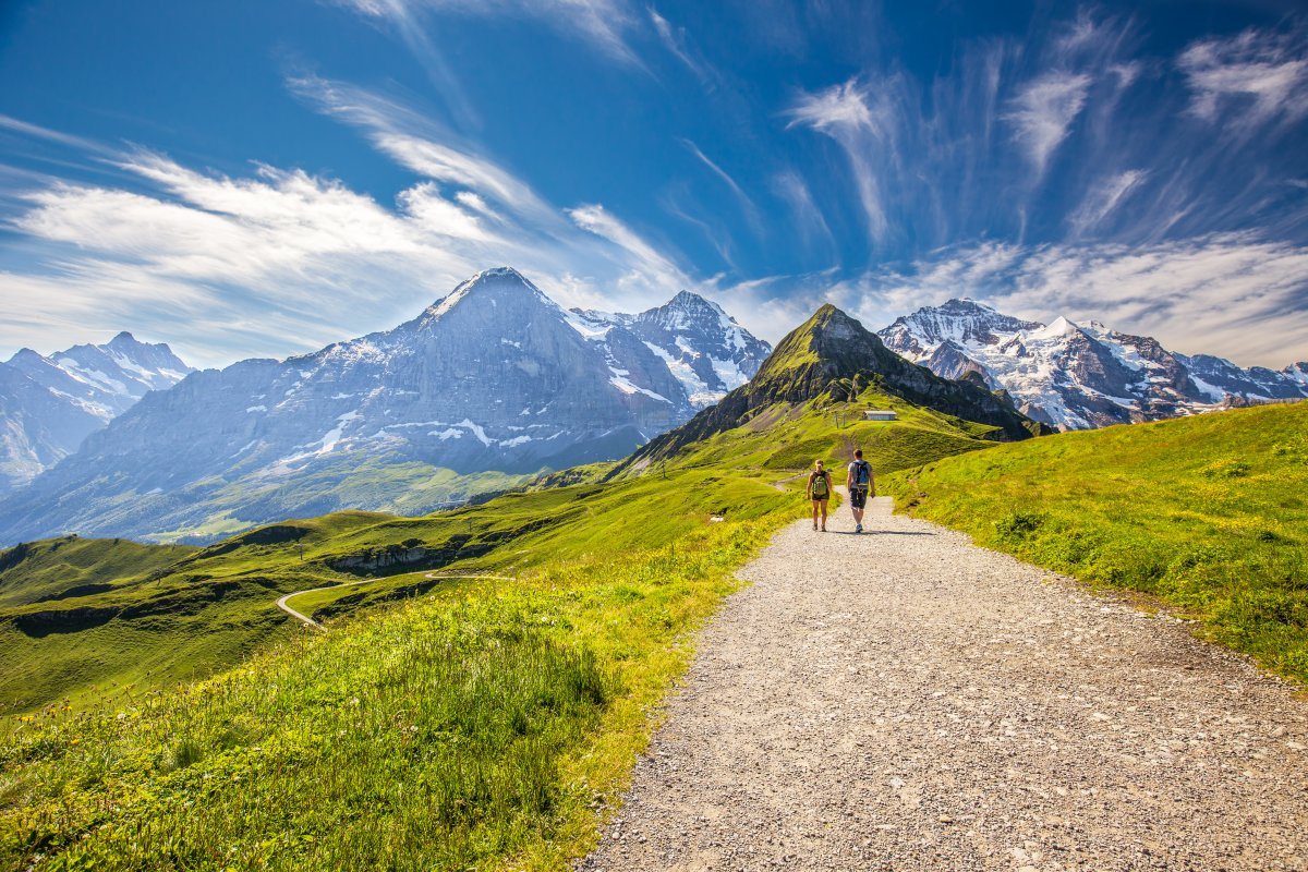 Young couple hiking in panorama trail leading to Kleine Scheidegg from Mannlichen with Eiger, Monch and Jungfrau mountain (Swiss Alps)