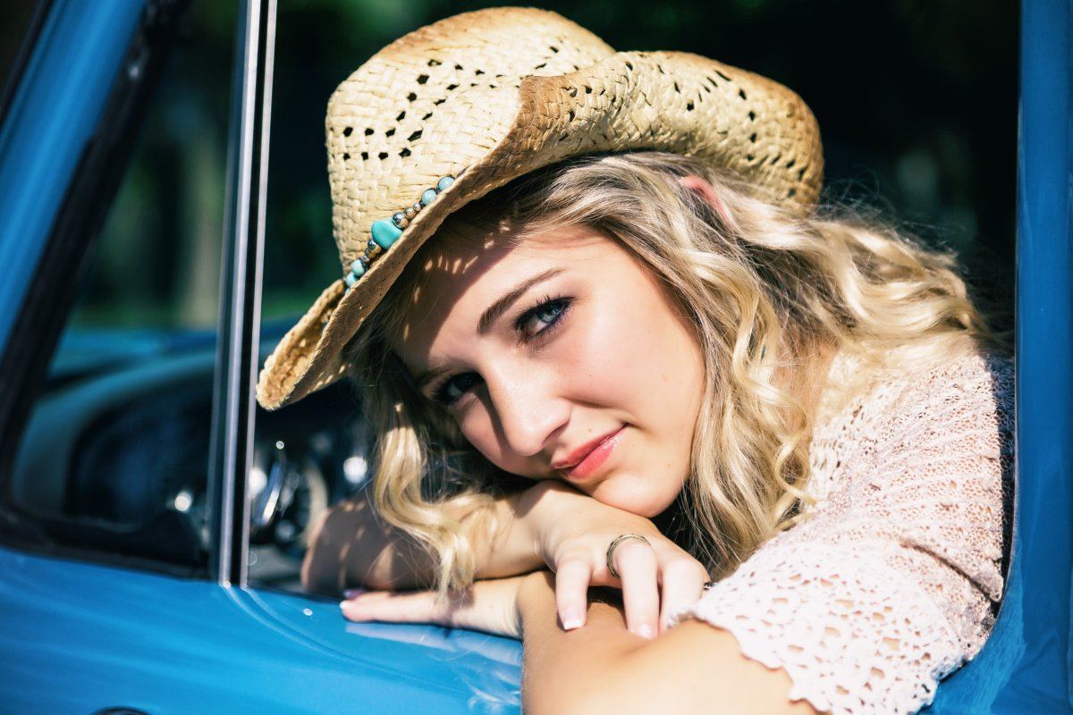 Beautiful Girl With Curly Blonde Hair Sitting In A Vintage Truck Wearing A Cowboy Hat.