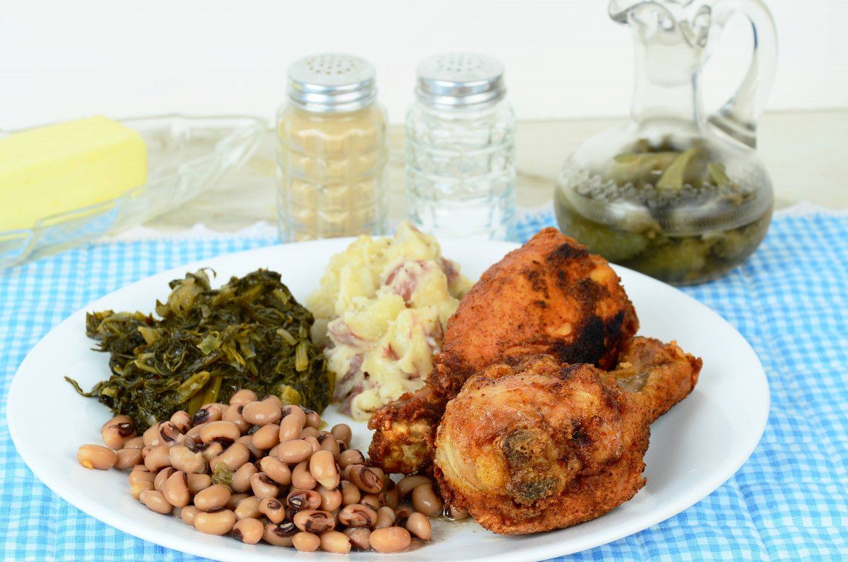 Black Eyed Peas And Turnip Greens With Deep Fried Chicken Legs And Potatoes And Spicy Vinegar Sauce On Blue Gingham Place Mat. Southern Cooking Where Dinner Is Often Called Supper.